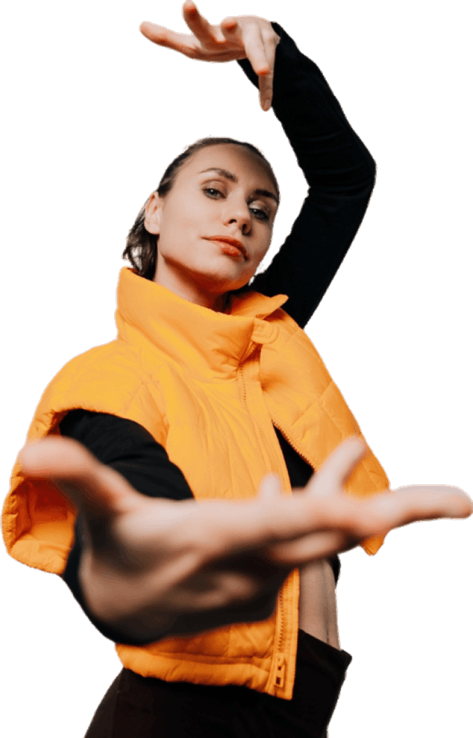 Человек в ярком оранжевом жилете и черной одежде выполняет танцевальное движение, протягивая руку вперед.